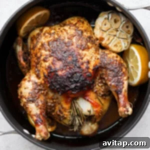 A perfectly roasted whole chicken, golden brown and garnished with fresh herbs, resting in a pan after cooking.