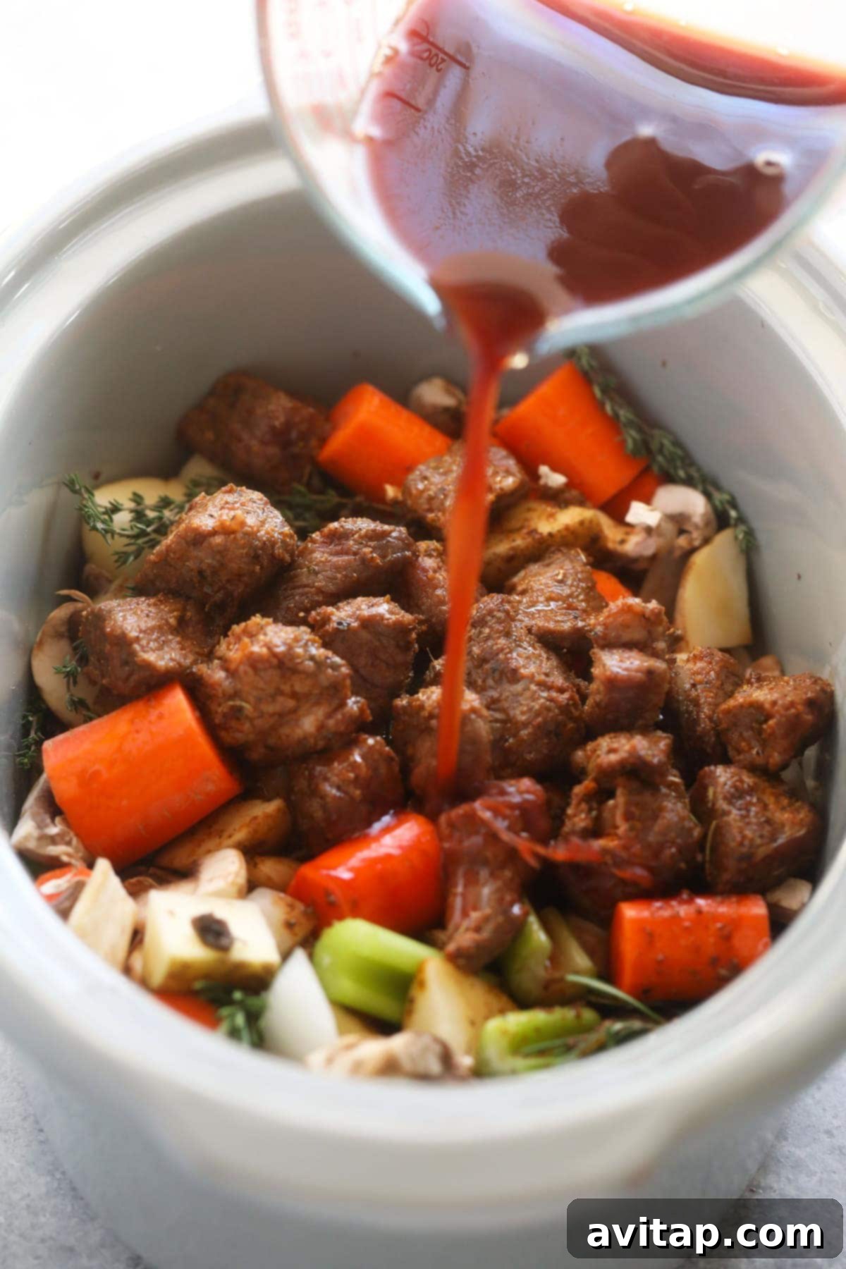 Slow cooker beef stew ingredients being gently mixed together in a slow cooker, showcasing the rich broth and colorful vegetables.