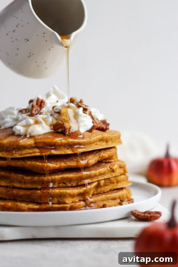 Healthy Pumpkin Pancakes with Whole Wheat Flour, Pumpkin Puree, Maple Syrup, and Pumpkin Pie Spice Stack of healthy pumpkin pancakes drizzled with syrup and topped with whipped cream.