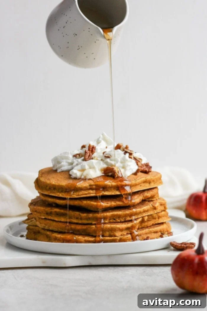 Maple Syrup Drizzled Over Fluffy Pumpkin Pancakes Pouring a generous amount of maple syrup over a stack of warm pumpkin pancakes.