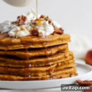 A stack of golden-brown pumpkin pancakes on a white plate, ready to be served.