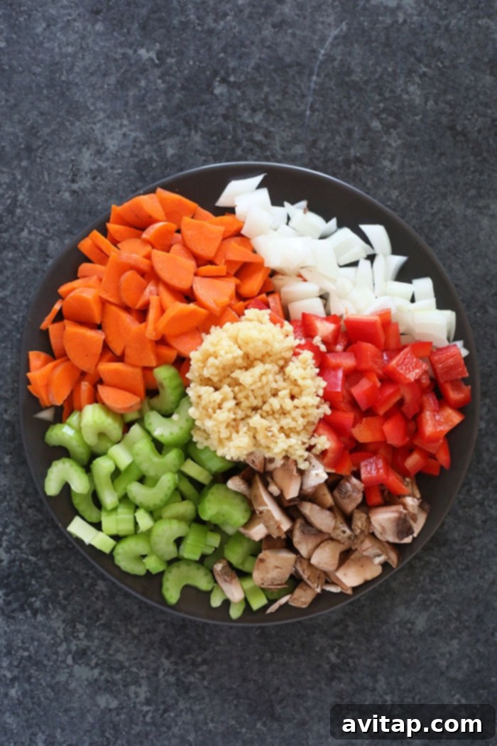An inviting assortment of fresh, colorful ingredients for Ramen Chicken Noodle Soup, including precisely diced carrots, crisp celery, aromatic onion, earthy mushrooms, pungent minced garlic, and vibrant red pepper, all artfully arranged on a rustic wooden board.