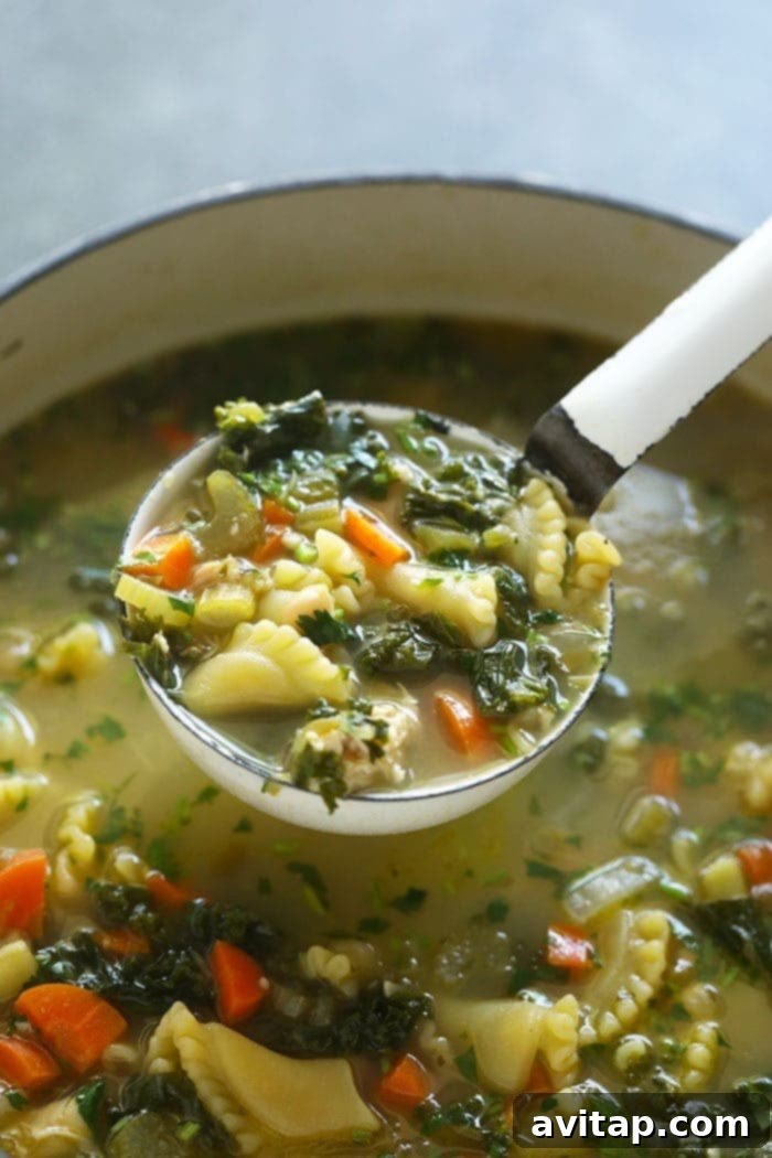 A ladle serving a generous portion of Green Monster Spicy Chicken Noodle Soup, highlighting the vibrant green kale and tender chicken pieces.