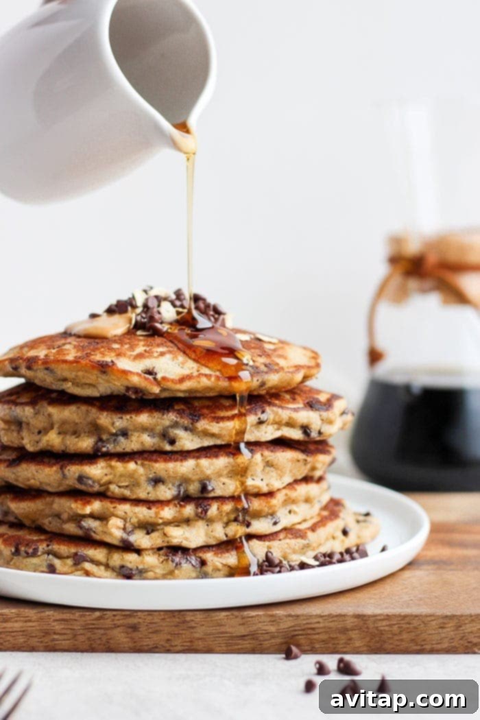 Fluffy Chocolate Chip Oatmeal Pancakes A beautifully arranged stack of golden-brown healthy chocolate chip pancakes drizzled with maple syrup