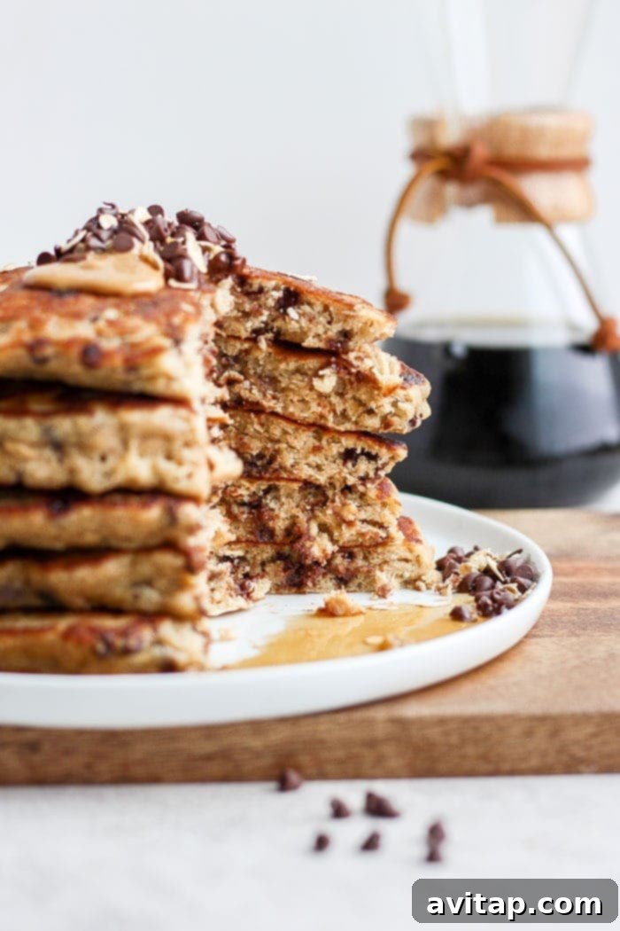 Perfectly Topped Healthy Pancakes Sliced stack of healthy chocolate chip oatmeal pancakes revealing fluffy interior, topped with maple syrup and fresh fruit