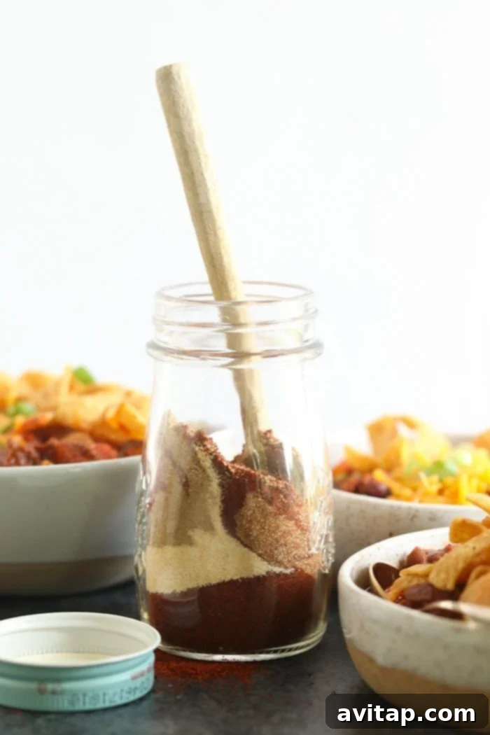 Homemade chili seasoning in a jar with a wooden spoon.