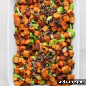 A white casserole dish filled with a colorful mix of cornbread dressing, wild rice, and vegetables, ready for the liquid.