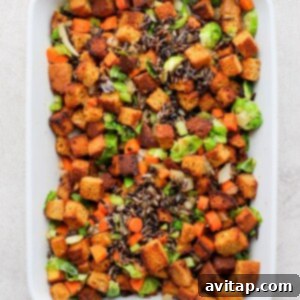 A white casserole dish filled with a mixture of cornbread croutons, wild rice, and colorful vegetables, before adding liquid.
