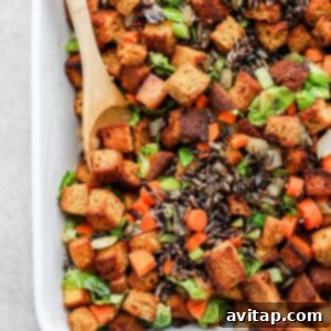 A freshly baked dish of cornbread dressing with visible carrots and Brussels sprouts, golden and bubbling.