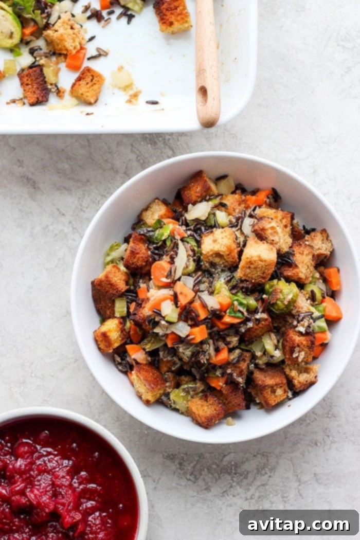 A bowl of homemade cornbread stuffing, garnished with fresh herbs, alongside a small bowl of cranberry sauce.