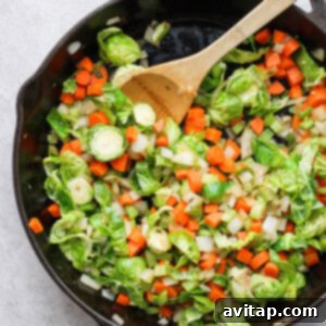 Brussels sprouts sautéed in a skillet with a wooden spoon, alongside other vegetables.