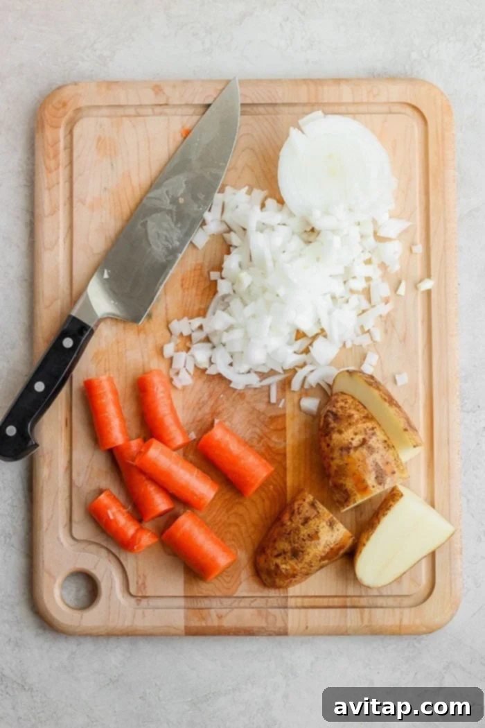 Freshly chopped potatoes, carrots, and onions on a cutting board, ready for the slow cooker.