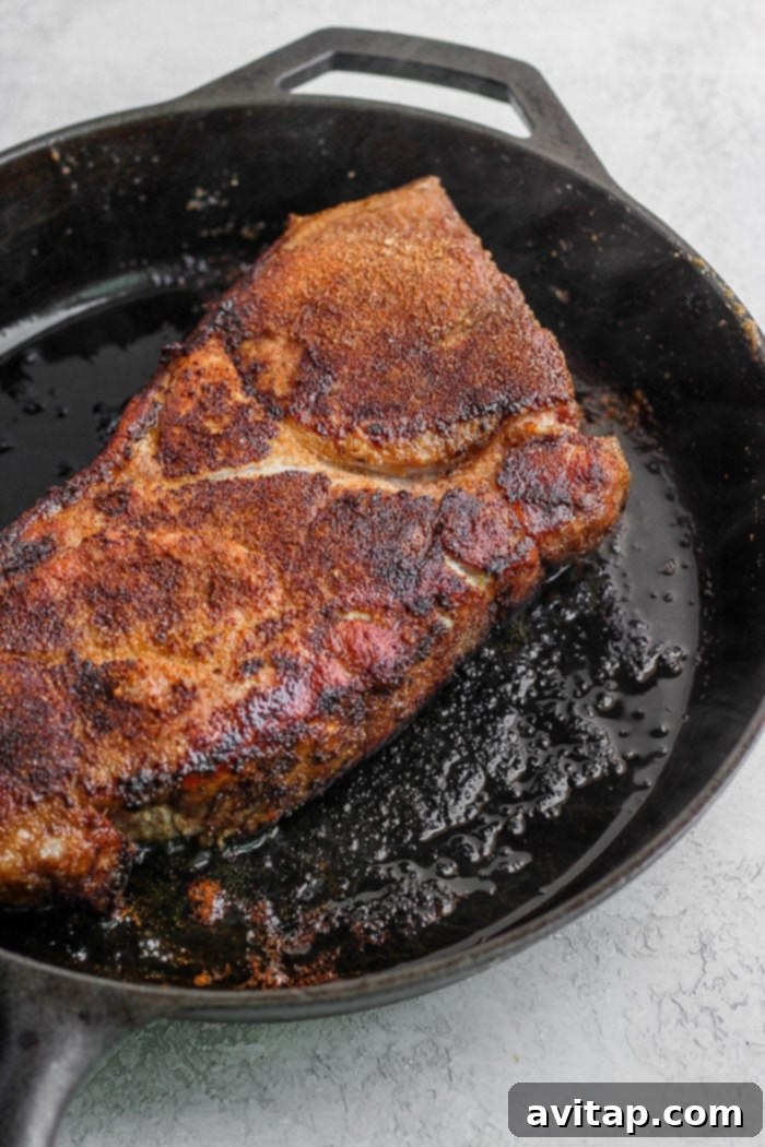 Pork roast being seared to a golden brown in a hot cast iron skillet.