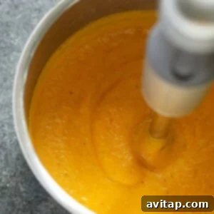 Butternut squash soup being pureed with an immersion blender in the pot.