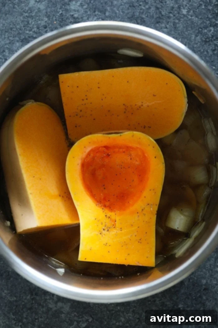 Quartered butternut squash placed inside the Instant Pot with sautéed aromatics.
