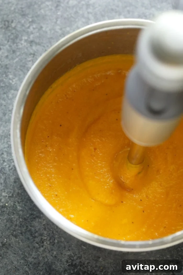 Creamy butternut squash soup being pureed directly in the Instant Pot using an immersion blender.