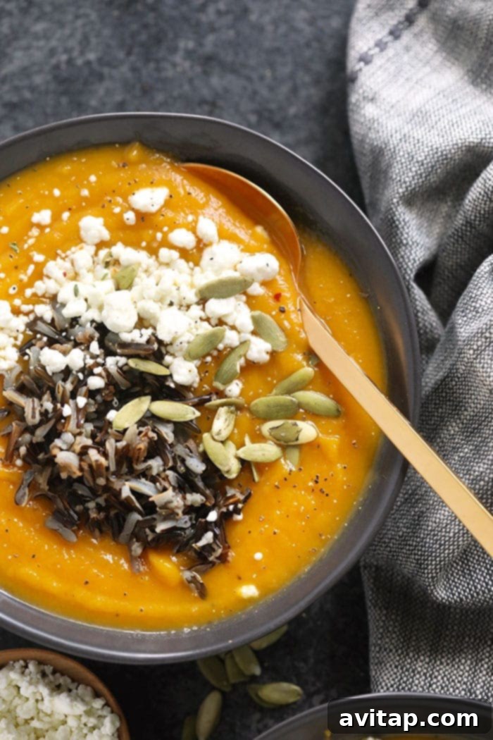 A bowl of Instant Pot Butternut Squash Soup, beautifully garnished with goat cheese, wild rice, and pepitas (pumpkin seeds).