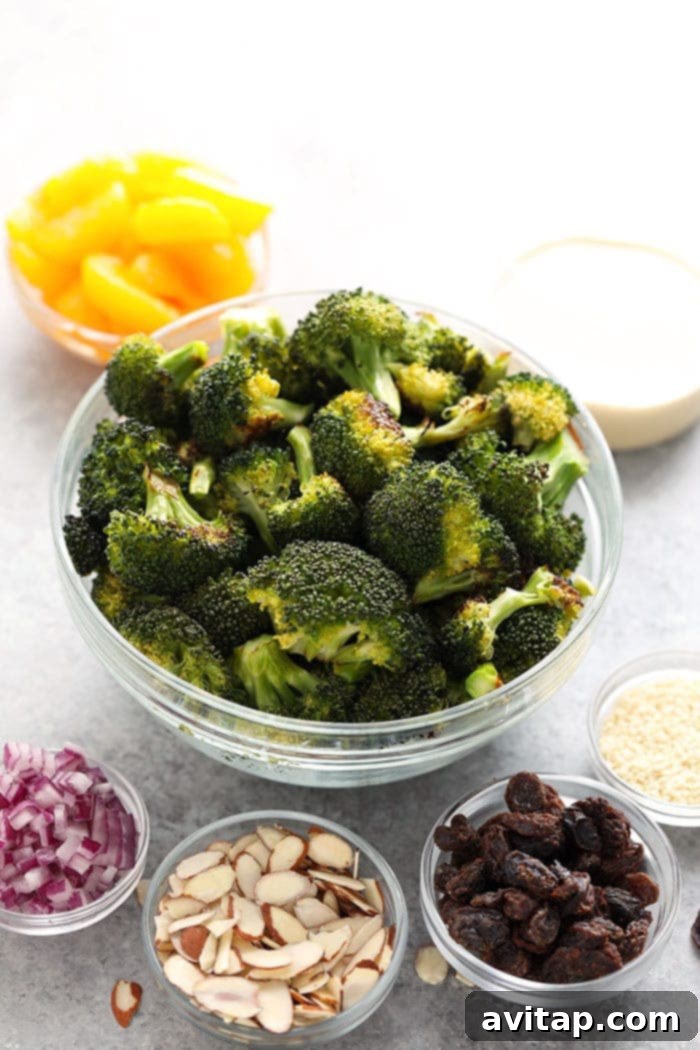 Individual ingredients for Asian Broccoli Salad laid out, including roasted broccoli, mandarin oranges, almonds, and red onion.