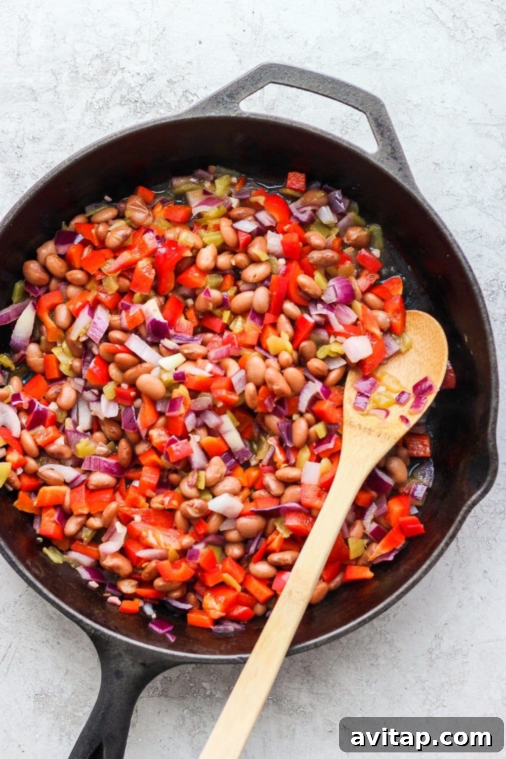 A colorful array of fresh ingredients for enchiladas laid out on a table, including shredded chicken, bell peppers, onions, beans, and tortillas.