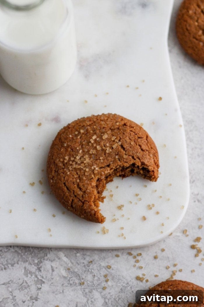 A perfectly baked ginger cookie with a piece bitten off, showcasing its tender, moist interior and golden-brown, crinkly exterior, glistening with turbinado sugar.