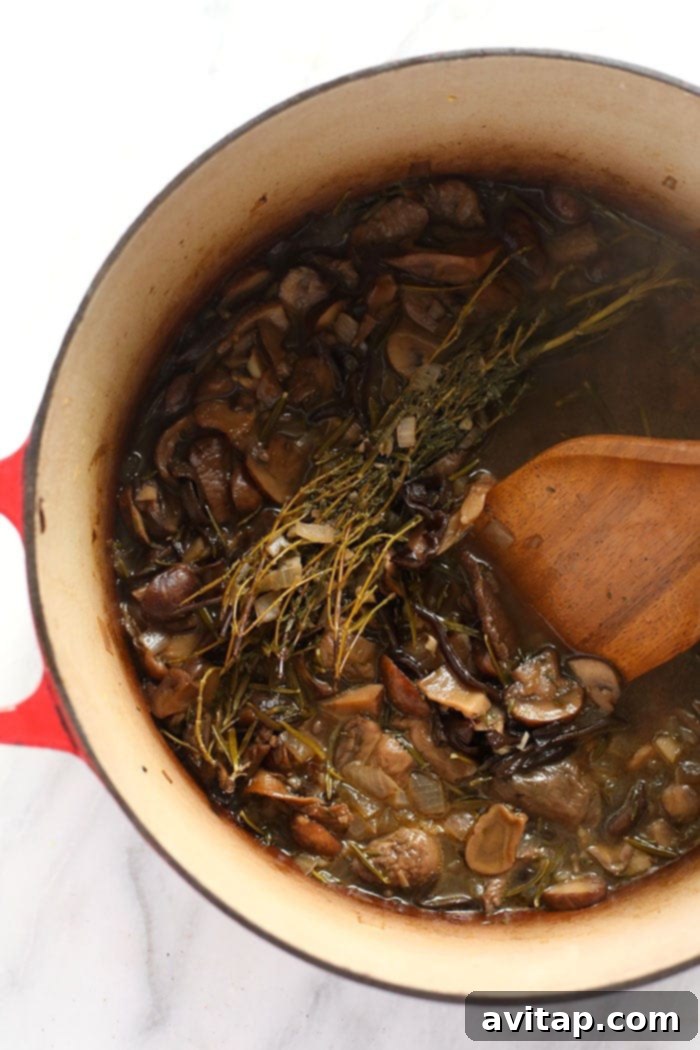 Rich mushroom gravy simmering and cooking down beautifully in a sturdy Dutch oven on the stovetop, showcasing the deep color and texture.