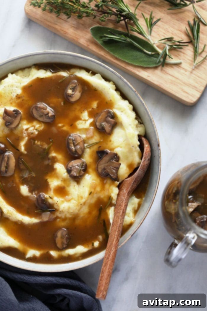 Delicious mushroom gravy generously drizzled over fluffy mashed potatoes in a white bowl, garnished with fresh herbs and ready to be served.