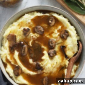 Vegan mashed potatoes with a generous topping of rich mushroom gravy, garnished with fresh herbs.