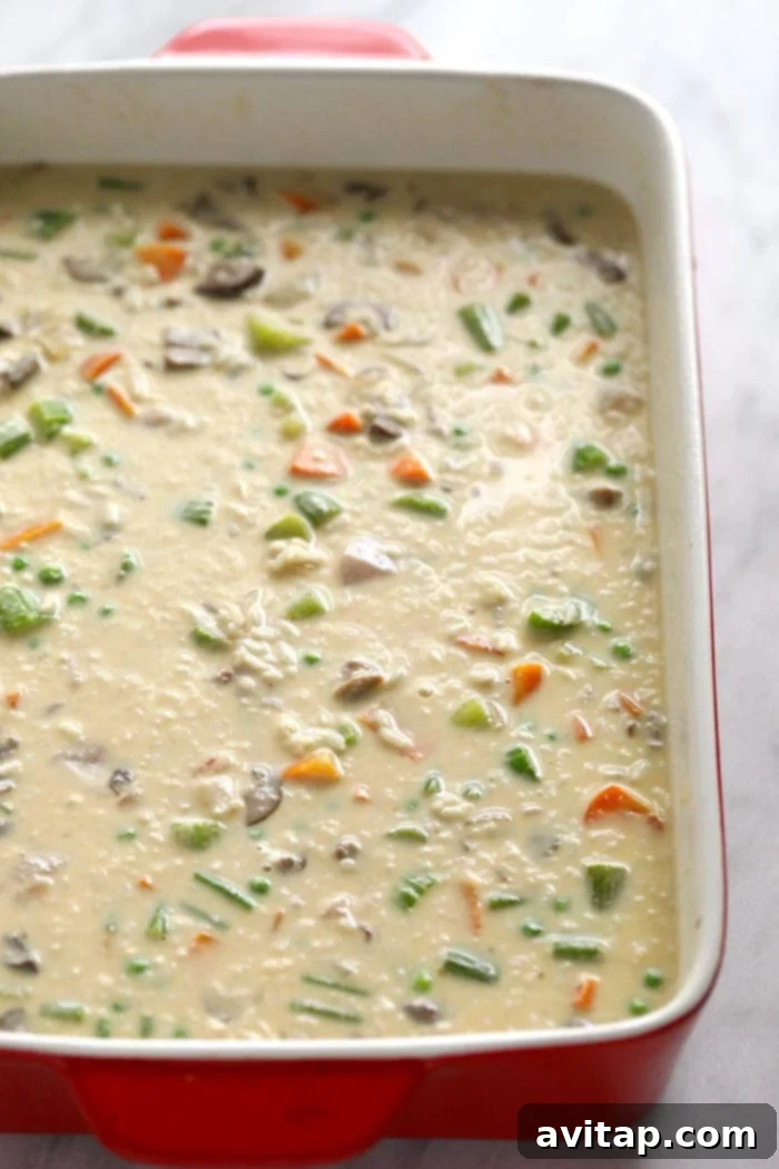 A close-up of a generous serving of creamy chicken pot pie casserole in a white bowl, showing tender chicken, peas, carrots, and the rich sauce.