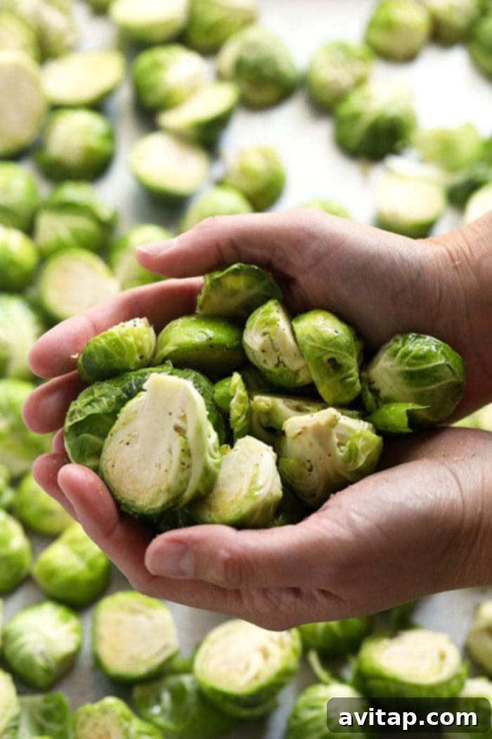 A close-up of a hand holding several freshly washed and halved Brussels sprouts, ready for seasoning and roasting.