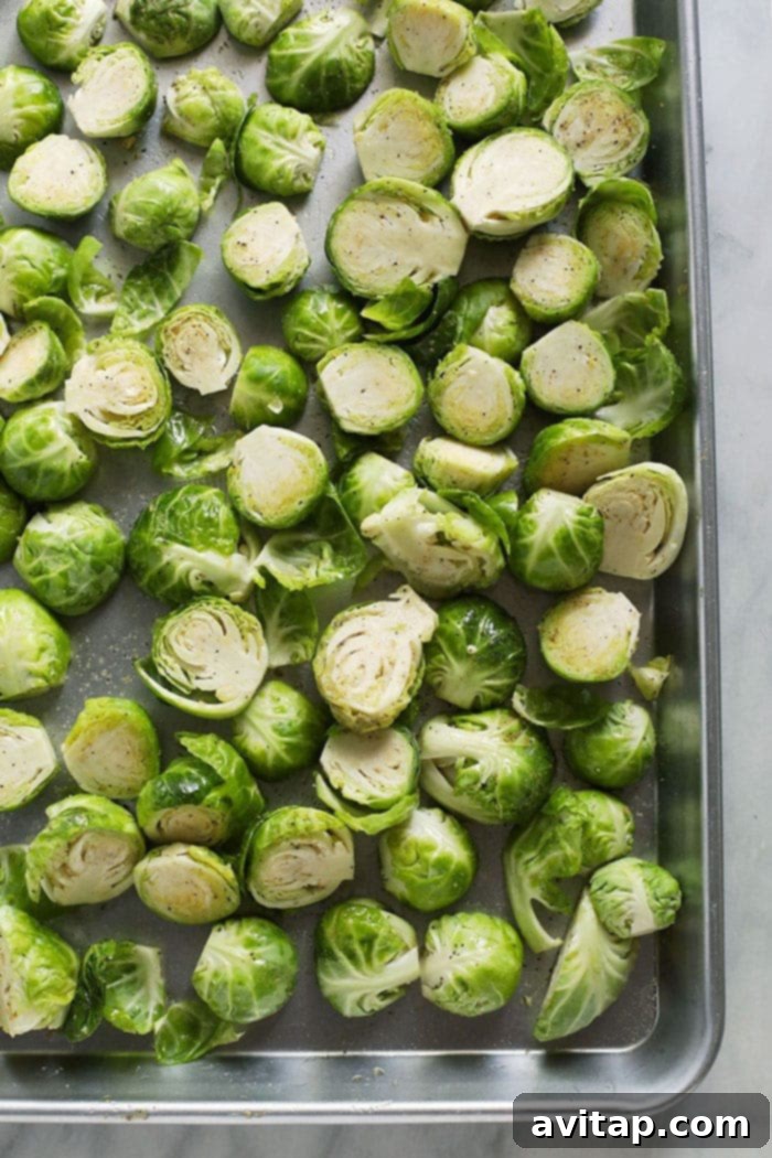 Halved Brussels sprouts seasoned with olive oil, salt, pepper, and garlic powder, spread in a single layer on a baking sheet, ready for roasting.