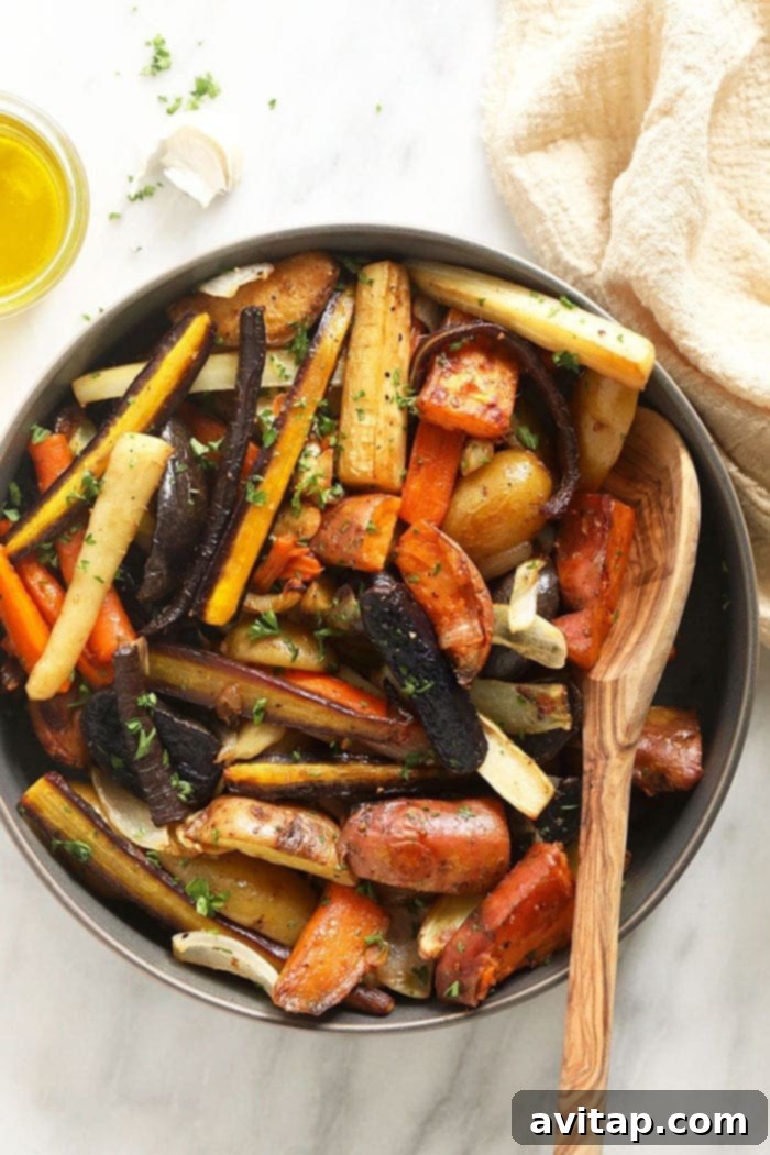 A bowl of golden brown, perfectly roasted root vegetables, garnished with fresh herbs, ready to be served with a spoon.
