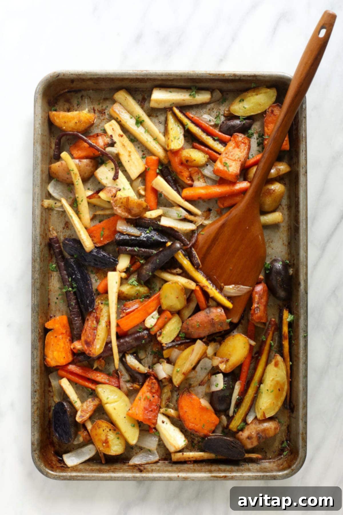 A baking sheet filled with a colorful array of roasted root vegetables, glistening with oil and seasonings, showcasing their golden-brown and slightly crispy textures.