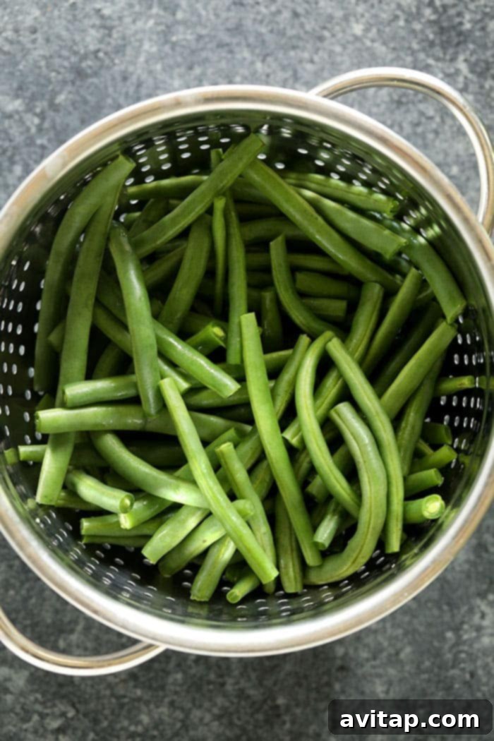 This Green Beans Almondine recipe starts by perfectly blanching fresh green beans, creating a delicious and buttery almond topping! Freshly blanched green beans draining in a colander, ready to be sautéed for almondine.