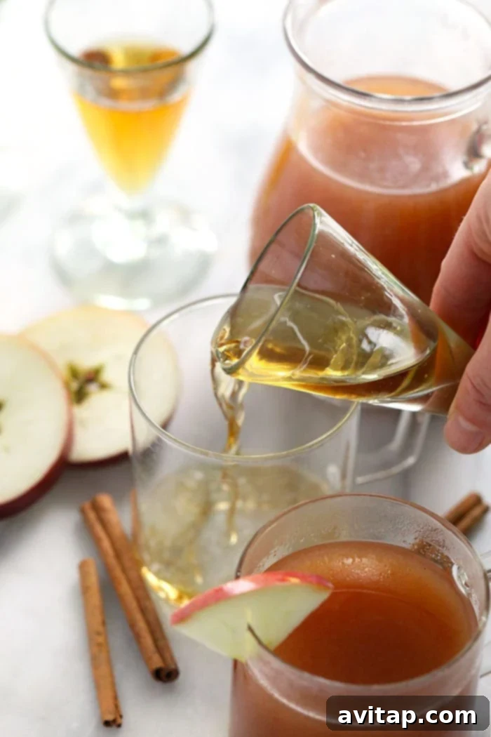 A shot of golden whiskey is skillfully poured into a warm mug of spiced apple cider, creating a rich and inviting fall cocktail, ready to be enjoyed.