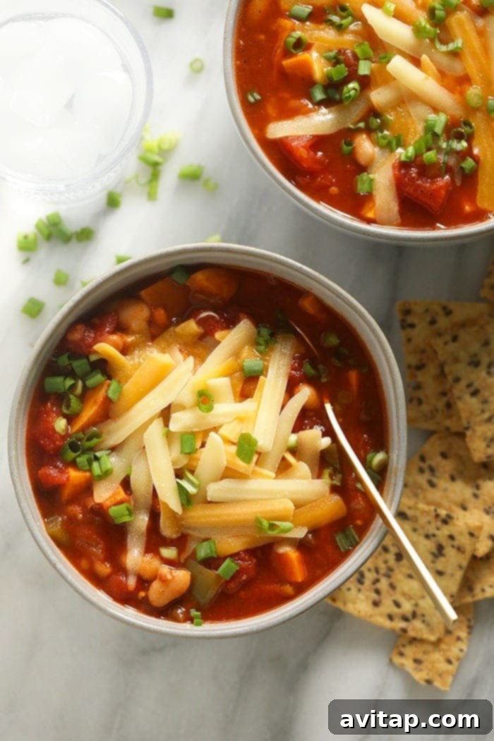A bowl of steaming vegetarian chili topped with shredded cheese and fresh green onions, showcasing a rich texture and inviting color.