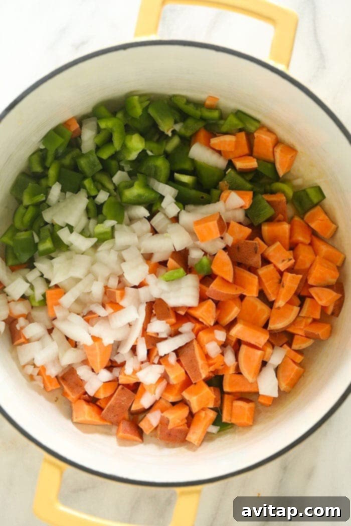 A vibrant mix of chopped onions, bell peppers, sweet potatoes, and other fresh vegetables being sautéed in a large stockpot.