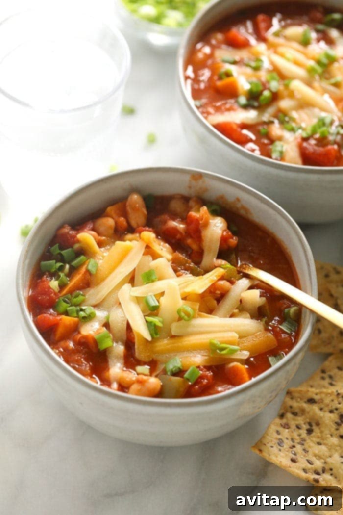 A close-up shot of a bowl of vegetarian chili, generously topped with melted shredded cheddar cheese and a sprinkle of green onions, ready to be enjoyed.