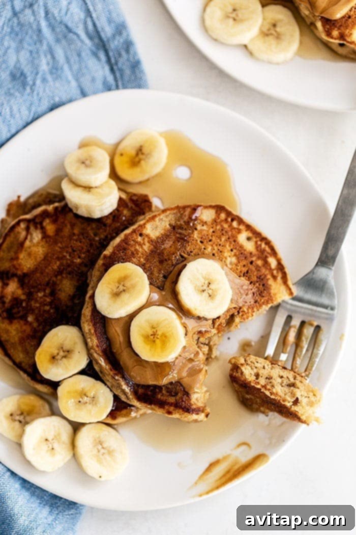 A stack of golden brown peanut butter banana pancakes drizzled with syrup and topped with fresh banana slices and chopped nuts, ready to be enjoyed.