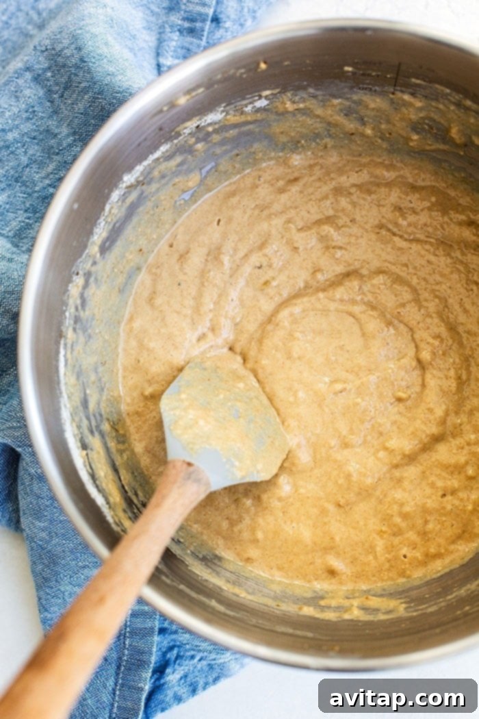 A bowl filled with a rich, creamy peanut butter banana pancake batter, showcasing its smooth consistency, with a whisk resting in it, ready for cooking.