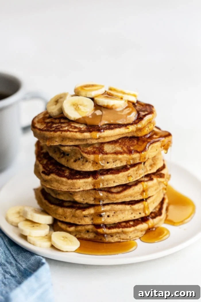 A close-up shot of a stack of fluffy peanut butter banana pancakes, topped with a generous drizzle of peanut butter and fresh banana slices, ready to be served.