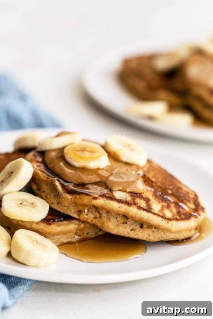 A plate featuring a stack of peanut butter banana pancakes, garnished with fresh fruit and a drizzle of syrup, presented as a ready-to-eat meal.