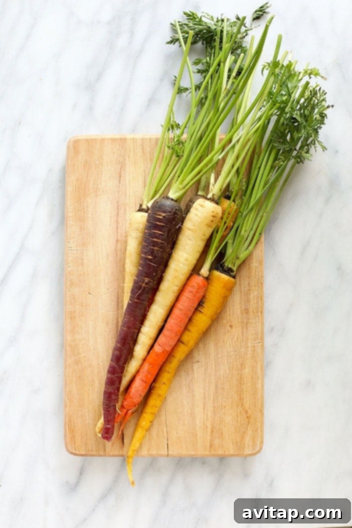 These Honey Balsamic Roasted Carrots are the ultimate holiday side dish! The combination of sweet and savory from the honey balsamic + perfectly roasted carrots, onions and garlic make this side a perfect addition to any holiday table. A vibrant selection of multi-colored carrots arranged on a cutting board, ready for preparation.