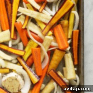 Carrots, onions, and garlic tossed with olive oil, salt, and pepper on a baking sheet, ready for the oven.