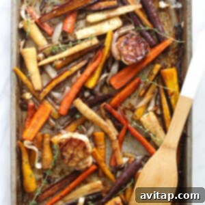 Roasted carrots and garlic on a baking sheet, being stirred with a wooden spoon, showcasing their golden caramelization.