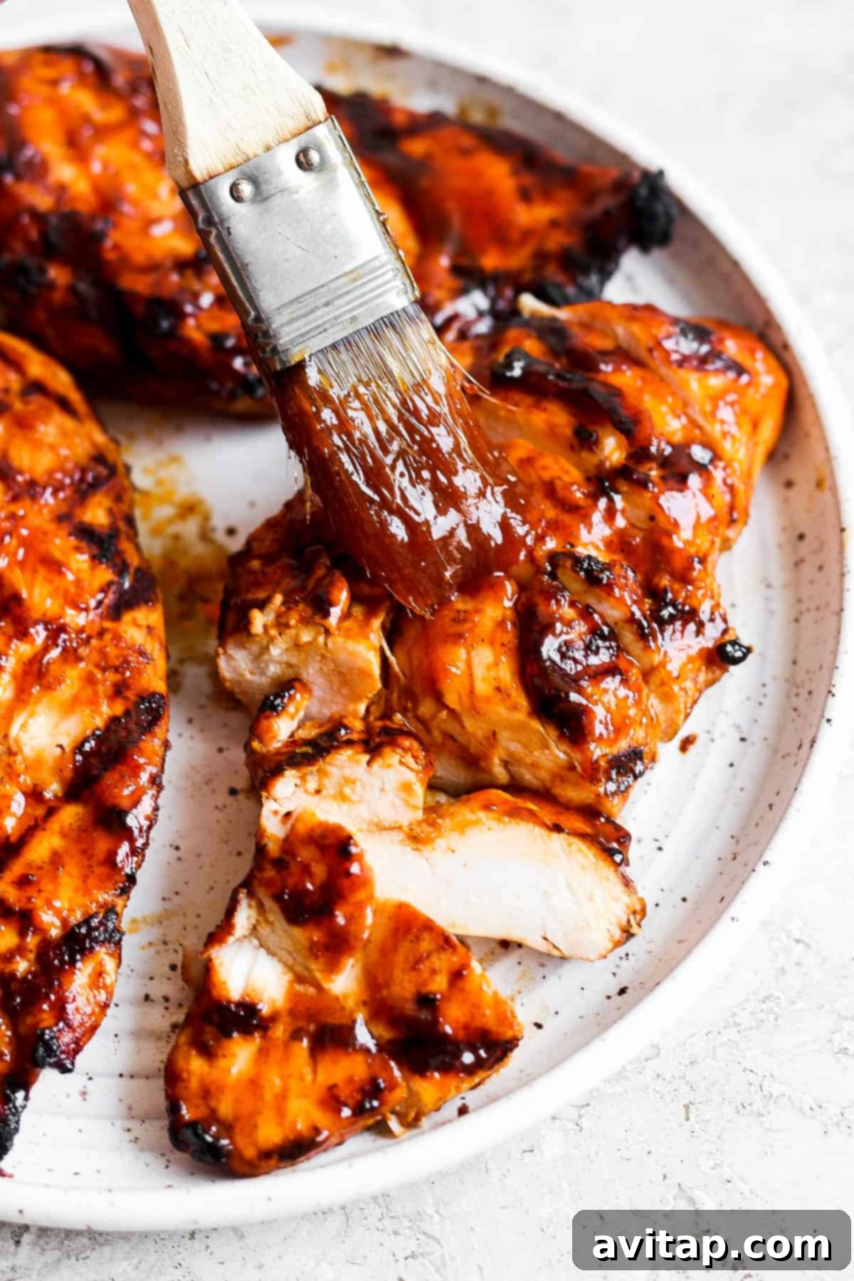 A freshly grilled BBQ chicken breast being brushed with extra BBQ sauce, ready to be sliced for the salad.