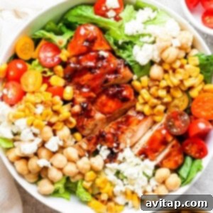A beautifully presented bowl of BBQ chicken salad with chickpeas and tomatoes, topped with fresh herbs.