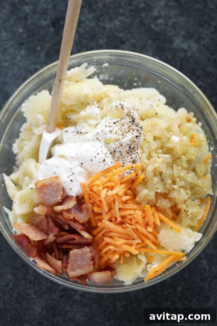 Creamy and Flavorful Twice Baked Potato Filling A large bowl filled with creamy twice baked potato filling, mixed with sautéed onions, garlic, and bacon bits, ready to be scooped into potato skins.