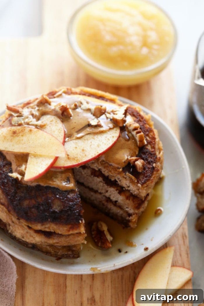 Applesauce pancakes on a plate topped with fresh apple slices and creamy nut butter, a perfect healthy and high-protein breakfast.
