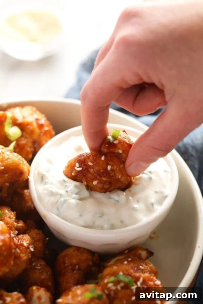 A sweet chili cauliflower wing being dipped into a creamy, vibrant sauce, highlighting its crispy texture.