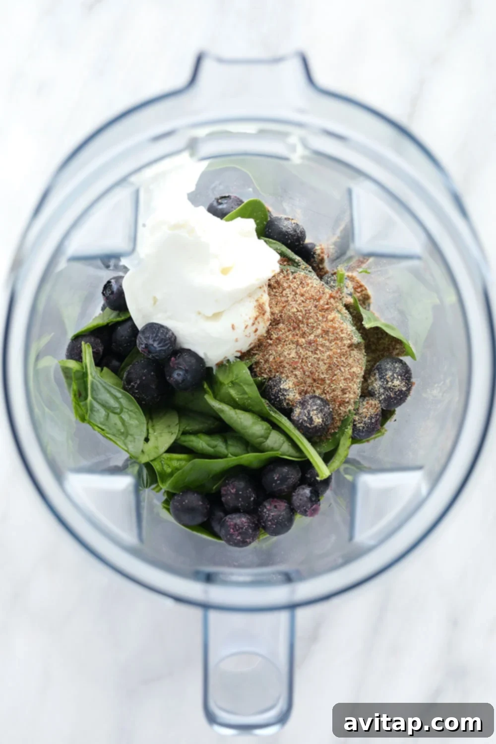 Fresh ingredients for a blueberry flax superfood smoothie arranged around a blender.